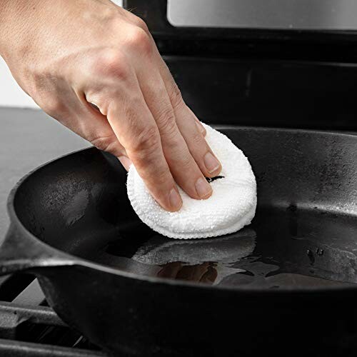 Hand cleaning a cast iron skillet with a white pad.