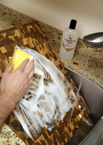 Person cleaning a wood cutting board with soap and water