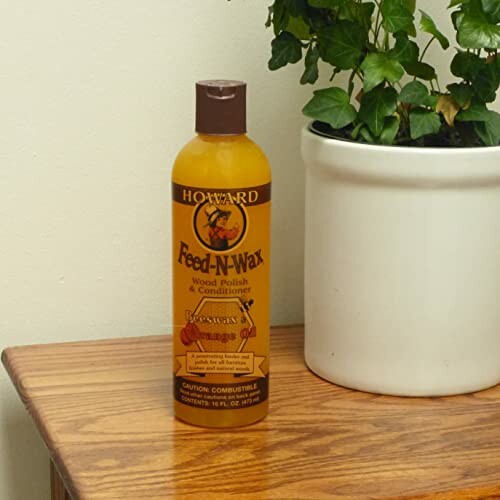 Howard Feed-N-Wax wood polish and conditioner bottle on wooden table beside potted plant