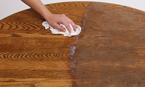 Hand cleaning wooden table with cloth showing before and after